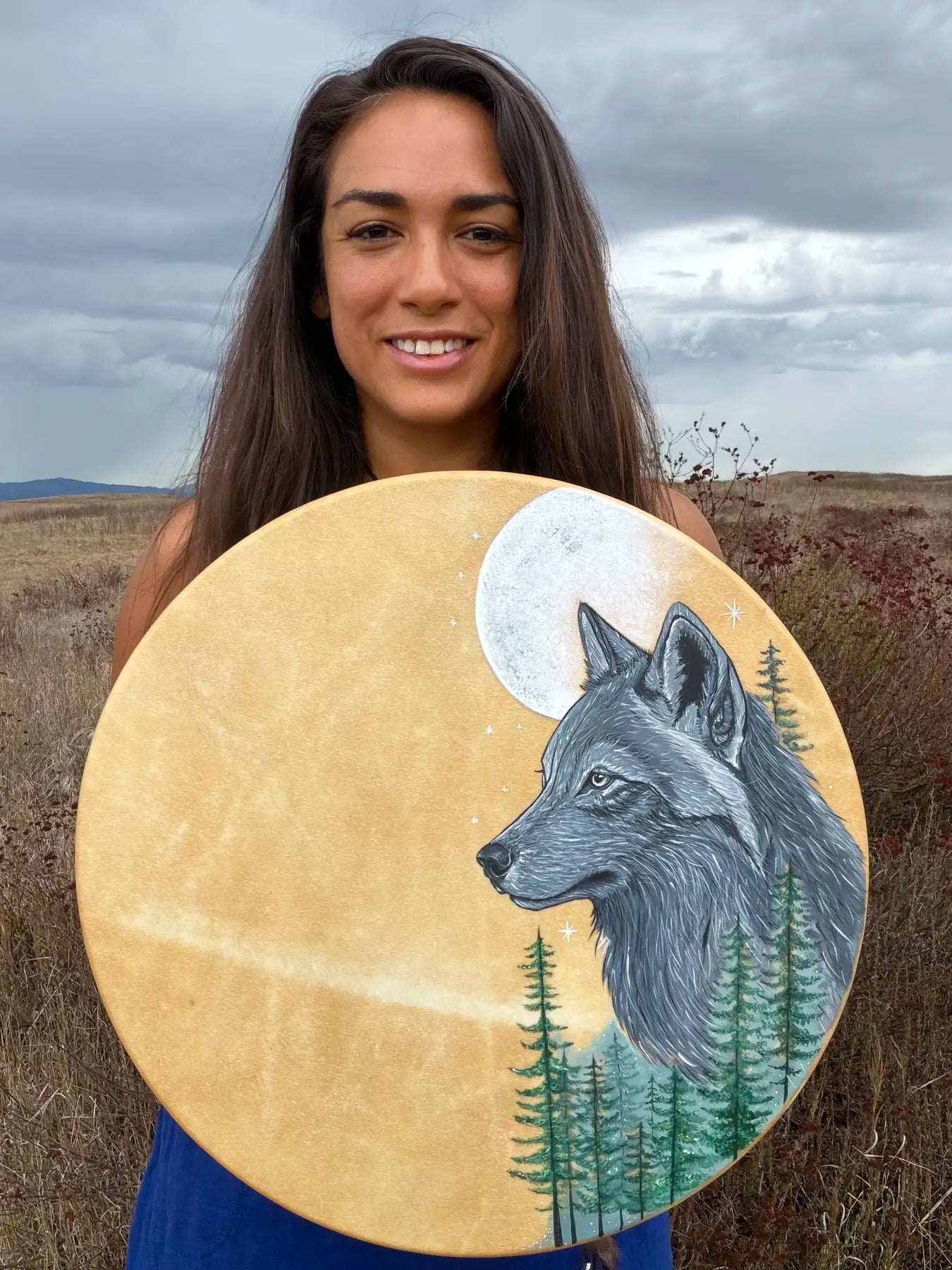 Niketa holding her handcrafted wolf and moon drum in a field